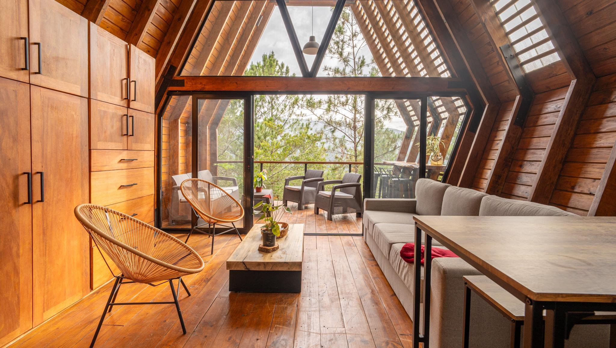 Warm wood-lined A-Frame great room opening onto a terrace with forest views